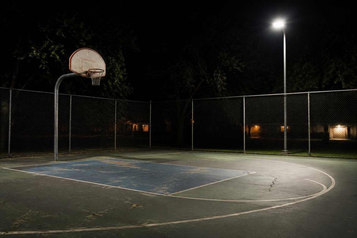 Een klein basketbalveld in de buurt, s avonds verlicht door een hoge lantaarnpaal.